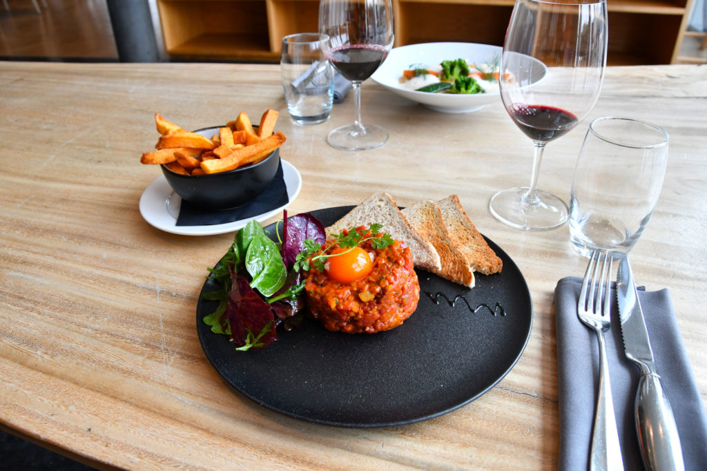 Un plat de tartare de bœuf accompagné de frites et d’un vin rouge.